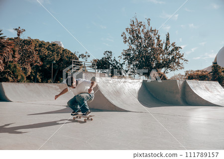 Active skateboarder jumping and performing a trick in a ramp of a skate park Active skateboarder jumping and performing a trick in a ramp of a skate park 111789157