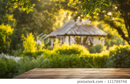 An empty wooden table in the foreground, with a blurred country house in the background against a verdant garden setting An empty wooden table in the foreground, with a blurred country house in the background against a verdant garden setting 111789748