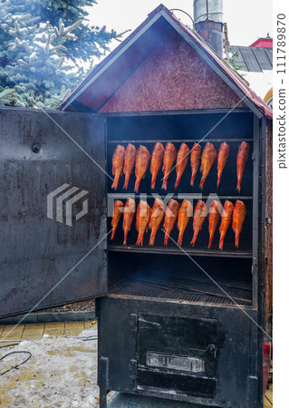 Appetizing fresh hot smoked red perch, sea bass fish hanging in a special outdoor metal smokehouse 111789870