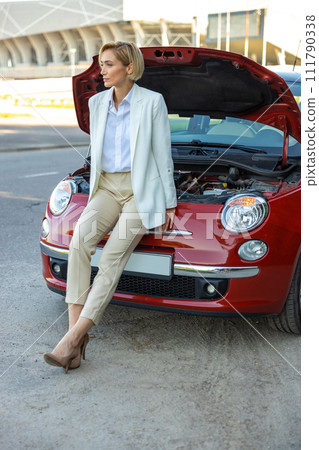 Woman standing near broken automobile on road waiting for service Woman standing near broken automobile on road waiting for service 111790338