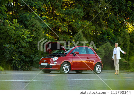 Woman standing near broken car on highway road asking for help from drivers raising her finger up Woman standing near broken car on highway road asking for help from drivers raising her finger up 111790344
