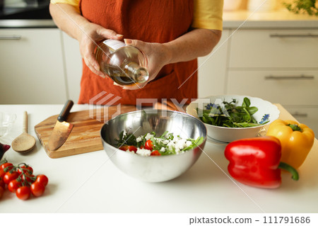 Female chef in a uniform pours olive oil from a bottle. Caucasian female food blogger working explaining how to cook a dish Female chef in a uniform pours olive oil from a bottle. Caucasian female food blogger working explaining how to cook a dish 111791686