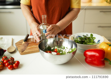 Close-up of a 60s woman preparing healthy vegetable salad in kitchen, seasoning meal, adding some herbs and salt to bowl, enjoying cooking vegetarian food at home, free space for advertising text 111791690
