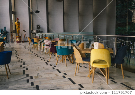 Modern white cafe interior with color tables with chairs standing next to them. Large windows and an empty wall. Modern white cafe interior with color tables with chairs standing next to them. Large windows and an empty wall. 111791707