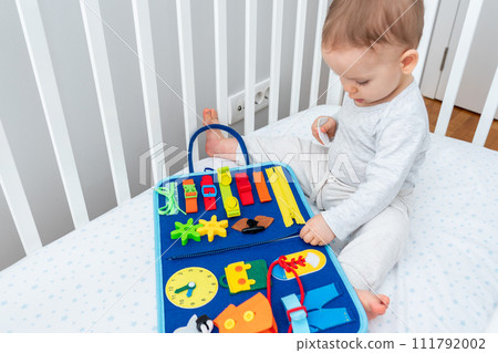 Baby playing with montessori quiet book sitting in a crib. Concept of smart books and modern educational toys Baby playing with montessori quiet book sitting in a crib. Concept of smart books and modern educational toys 111792002