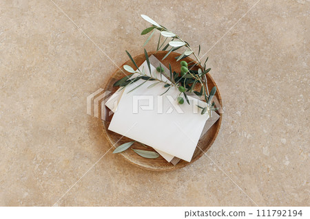Mediterranean summer stationery still life. Empty greeting card mockup on wooden plate. Olive tree branches on golden marble background. Wedding invitation. Flat lay, top view. Minimal design, nobody. 111792194