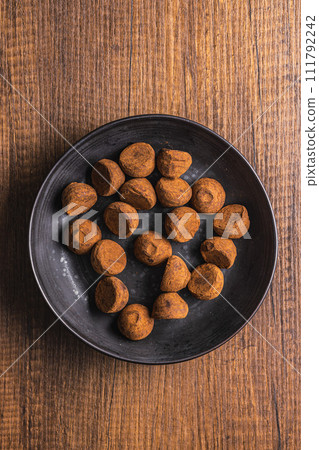 Chocolate truffles covered with cocoa powder on plate on wooden table. Top view. Chocolate truffles covered with cocoa powder on plate on wooden table. Top view. 111792242