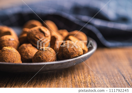 Chocolate truffles covered with cocoa powder on plate on wooden table. Chocolate truffles covered with cocoa powder on plate on wooden table. 111792245