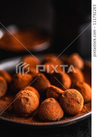 Chocolate truffles covered with cocoa powder on plate on black table. Chocolate truffles covered with cocoa powder on plate on black table. 111792263