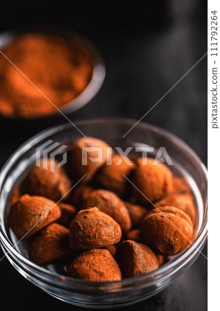 Chocolate truffles covered with cocoa powder in bowl on black table. Chocolate truffles covered with cocoa powder in bowl on black table. 111792264