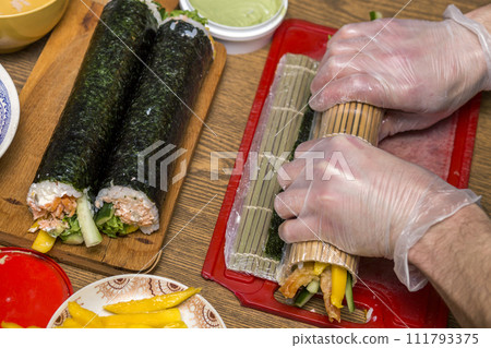 Process of making sushi and rolls. Close-up of man chef hands preparing traditional Japanese food at home or in restaurant on kitchen table. Process of making sushi and rolls. Close-up of man chef hands preparing traditional Japanese food at home or in restaurant on kitchen table. 111793375