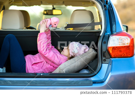Pretty happy child girl playing with a pink toy teddy bear in a car trunk. Pretty happy child girl playing with a pink toy teddy bear in a car trunk. 111793378