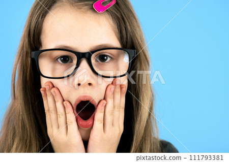 Portrait of surprised child girl wearing looking glasses holding hands to her face isolated on blue background. 111793381