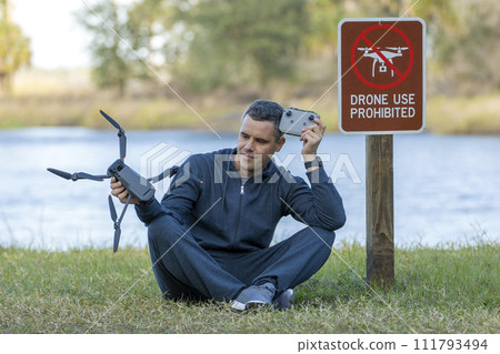 Man is sad that he is not allowed to fly his quadcopter state park no drone area. Operator is unauthorised to use UAS near restriction sign Man is sad that he is not allowed to fly his quadcopter state park no drone area. Operator is unauthorised to use UAS near restriction sign 111793494