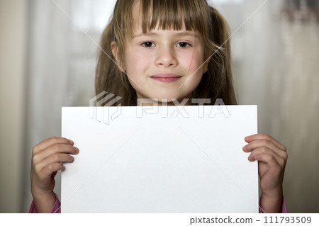 Happy smiling cute child girl holding white copy space sheet of drawing paper. Art education, creativity, advertisement concept. 111793509