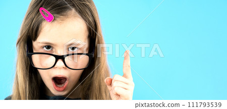 Close up portrait of a child school girl wearing looking glasses holding up point finger in I have an idea gesture isolated on blue background. 111793539