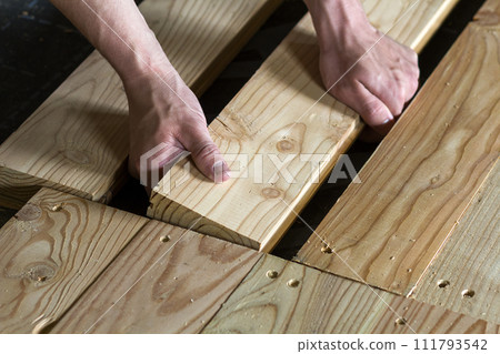 Close up of strong muscular hands of professional carpenter installing natural wooden new planks on wooden frame floor Reconstruction, improvement, renovation and carpentry concept. 111793542