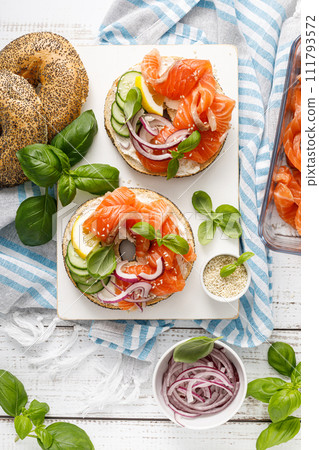Salmon sandwiches with bagel, salted fish, fresh cucmber, onion and basil on white background, top view. Healthy breakfast with salmon toasts Salmon sandwiches with bagel, salted fish, fresh cucmber, onion and basil on white background, top view. Healthy breakfast with salmon toasts 111793572