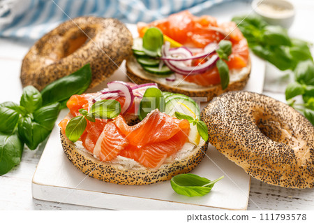 Salmon sandwiches with bagel, salted fish, fresh cucmber, onion and basil on white background. Healthy breakfast with salmon toasts 111793578