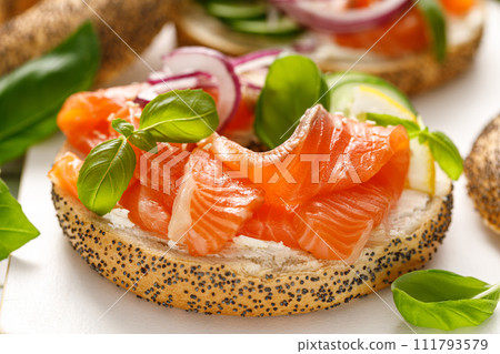 Salmon sandwiches with bagel, salted fish, fresh cucmber, onion and basil on white background. Healthy breakfast with salmon toasts 111793579