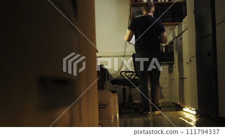 Rear view of a man walking towards an opened drawer against reception desk. Stock footage. Interior of a small hostel with reception and a fridge, cheap accommodation concept. Rear view of a man walking towards an opened drawer against reception desk. Stock footage. Interior of a small hostel with reception and a fridge, cheap accommodation concept. 111794337