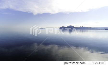 Beautiful sunrise and the morning haze hanging above the lake. Shot. Amazing blue sky and calm water, fog, and silhouettes of hills. Beautiful sunrise and the morning haze hanging above the lake. Shot. Amazing blue sky and calm water, fog, and silhouettes of hills. 111794409