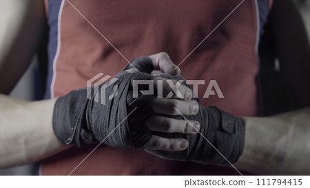 Man flexing his fists before a fight. Close-up of a young Thai boxer hands hemp ropes are wrapped before the fight or training Man flexing his fists before a fight. Close-up of a young Thai boxer hands hemp ropes are wrapped before the fight or training 111794415