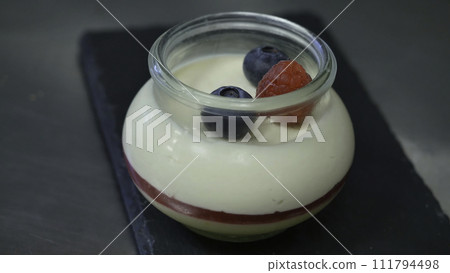 Homemade yogurt with blueberries in a glass jar. Hand putting Strawberry in Yogurt, close up 111794498