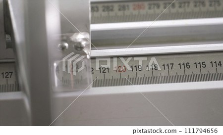 Close-up of worker of furniture factory measuring a wooden block with industrial measuring device. Action. Production, manufacture and woodworking industry concept 111794656