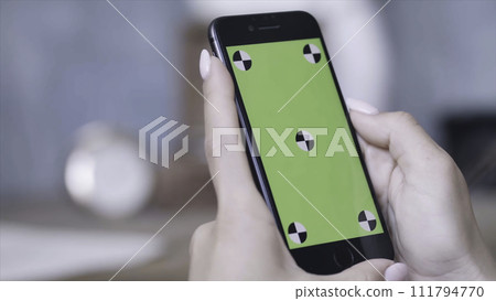Close-up of young woman's hands with perfect manicure holding smartphone and sliding on the chroma key green screen. Stock footage. Chroma key screen for placement of your own content. Close-up of young woman's hands with perfect manicure holding smartphone and sliding on the chroma key green screen. Stock footage. Chroma key screen for placement of your own content. 111794770