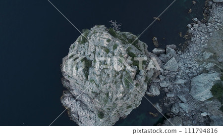 Magnificent sea with dark blue water and impregnable rocks covered with green trees and bushes. Shot. Top view of steep cliff and the sea coast with small soft ripples. 111794816
