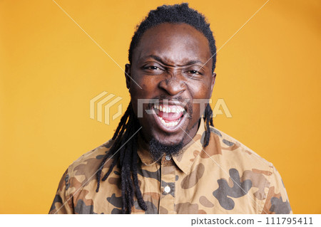 Furious stressed man having breakdown while posing aggresive in studio over yellow background, showing unpleasant reaction. African american young adult feeling frustrated and mad 111795411