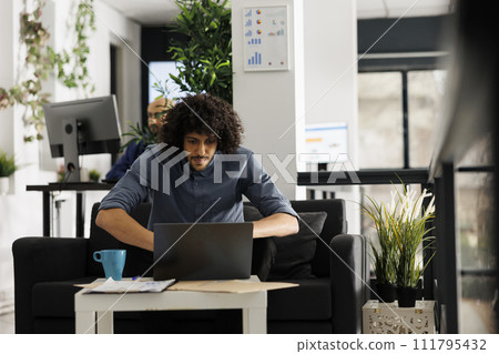 Young arab entrepreneur analyzing company sales statistics on laptop while working in business office. Start up employee managing project and checking corporate marketing research 111795432