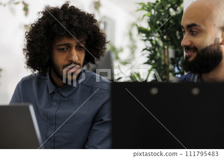 Coworkers brainstorming and planning marketing campaign on laptop while working in business office. Arab entrepreneurs analyzing sales result data on computer in coworking space 111795483