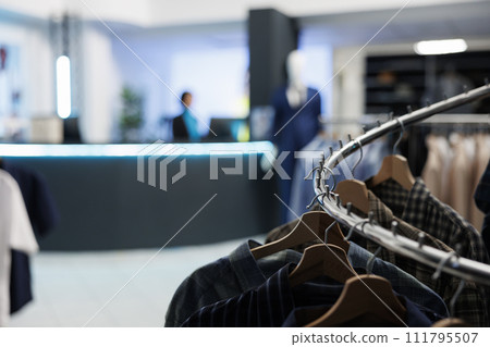 Apparel rack closeup in empty clothing store outlet with blurred background. Trendy stylish casual garment hanging in shopping center fashion boutique with no people indoors 111795507