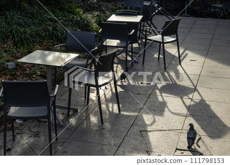Empty tables and chairs shadows outside a cafe and pigeon on the pavement. Empty tables and chairs shadows outside a cafe and pigeon on the pavement. 111798153