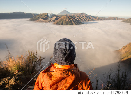 Back view of tourist standing on the hill and looking to the beautiful sunrise and sea of fog over Bromo Tengger Semeru National Park in East Java, Indonesia. 111798729