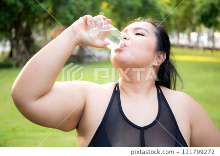 Active plus size woman hydration drinking a water bottle outdoors. Active plus size woman hydration drinking a water bottle outdoors. 111799272