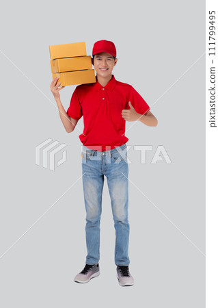 Young asian man in uniform red and cap carrying box stack and gesture thumbs up isolated. Young asian man in uniform red and cap carrying box stack and gesture thumbs up isolated. 111799495
