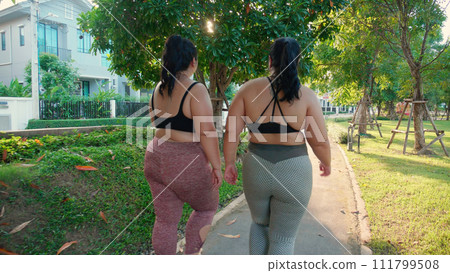 Two asian woman fat in sportswear jogging together on pathway at park. Two asian woman fat in sportswear jogging together on pathway at park. 111799508