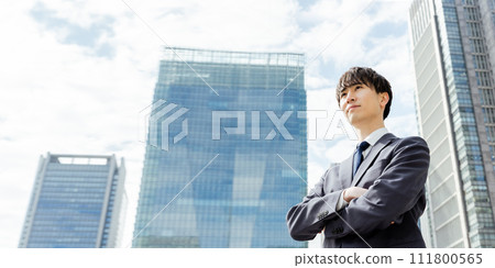 A man in his 20s in a suit opens his notebook outdoors and checks the contents with a serious expression A man in his 20s in a suit opens his notebook outdoors and checks the contents with a serious expression 111800565