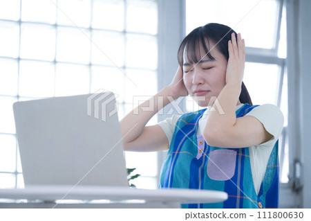 A woman with a tired expression in front of a computer - Image of overtime for childcare workers and caregivers 111800630