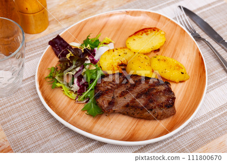 Grilled beef steak with baked potato slices garnished with greens 111800670