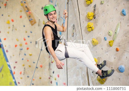 Confident young man wearing helmet scaling artificial climbing wall in climbing gym Confident young man wearing helmet scaling artificial climbing wall in climbing gym 111800731