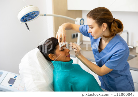 Female cosmetologist marking skin of hispanic with white pencil Female cosmetologist marking skin of hispanic with white pencil 111800843