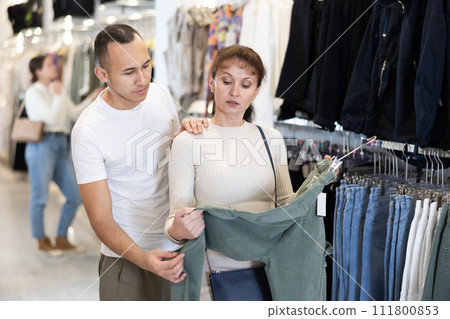 Young couple choosing casual pants in clothing store Young couple choosing casual pants in clothing store 111800853