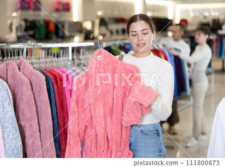 Young woman choosing bathrobe in store 111800873