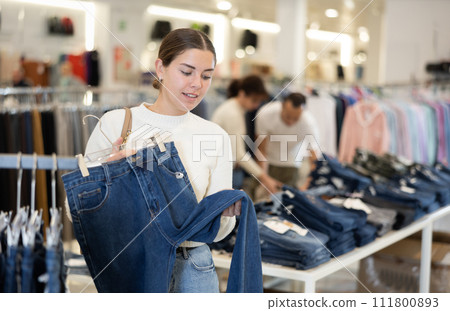 Young girl choosing blue jeans in clothing store Young girl choosing blue jeans in clothing store 111800893