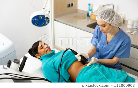 Cosmetologist performing ultrasound cavitation body procedure for client 111800908