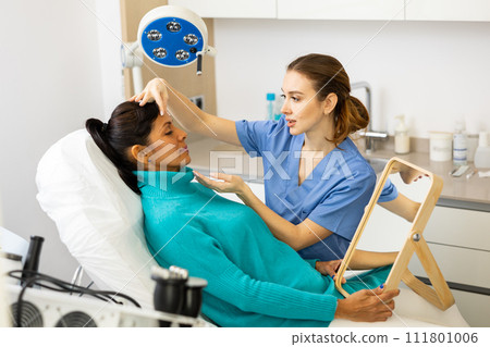 Beautician examining face skin of female patient Beautician examining face skin of female patient 111801006